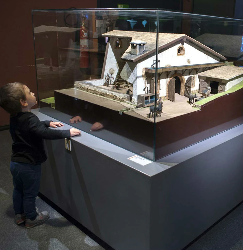 A young child looks at a detailed house model displayed in a glass case at a museum.