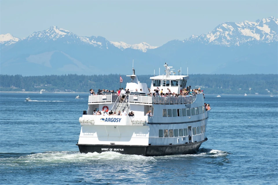 Argosy Cruise boat cruising towards Olympic Mountains, with people visible on the outer decks