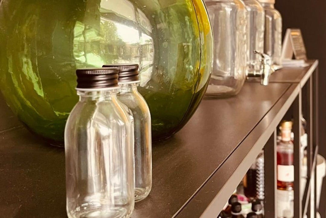 棚の大きな緑色のガラスの水差しと透明なガラス容器の前には、黒いキャップの付いた小さなガラス瓶が2つあります。
