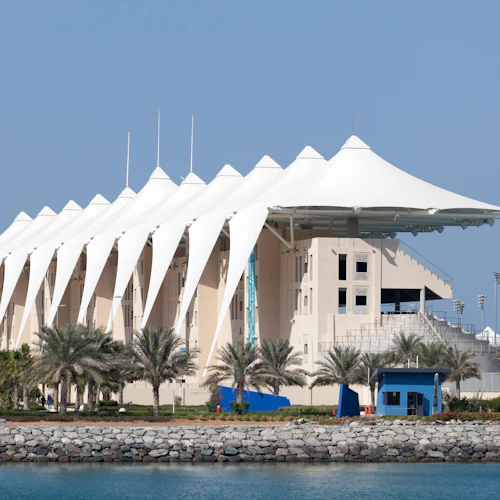 Ein großes Gebäude am Wasser mit einem weißen zeltartigen Dach, umgeben von Palmen und einer felsigen Küste unter einem klaren blauen Himmel.