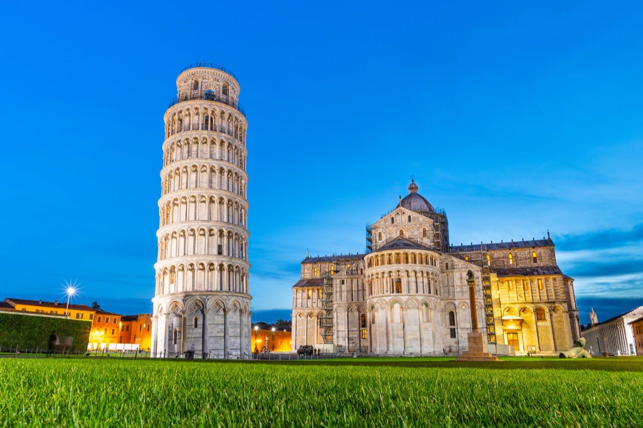 Ο κεκλιμένος πύργος της Πίζας και ο καθεδρικός ναός της Πίζας το σούρουπο με καθαρό ουρανό, όπως φαίνεται από ένα καταπράσινο γρασίδι.