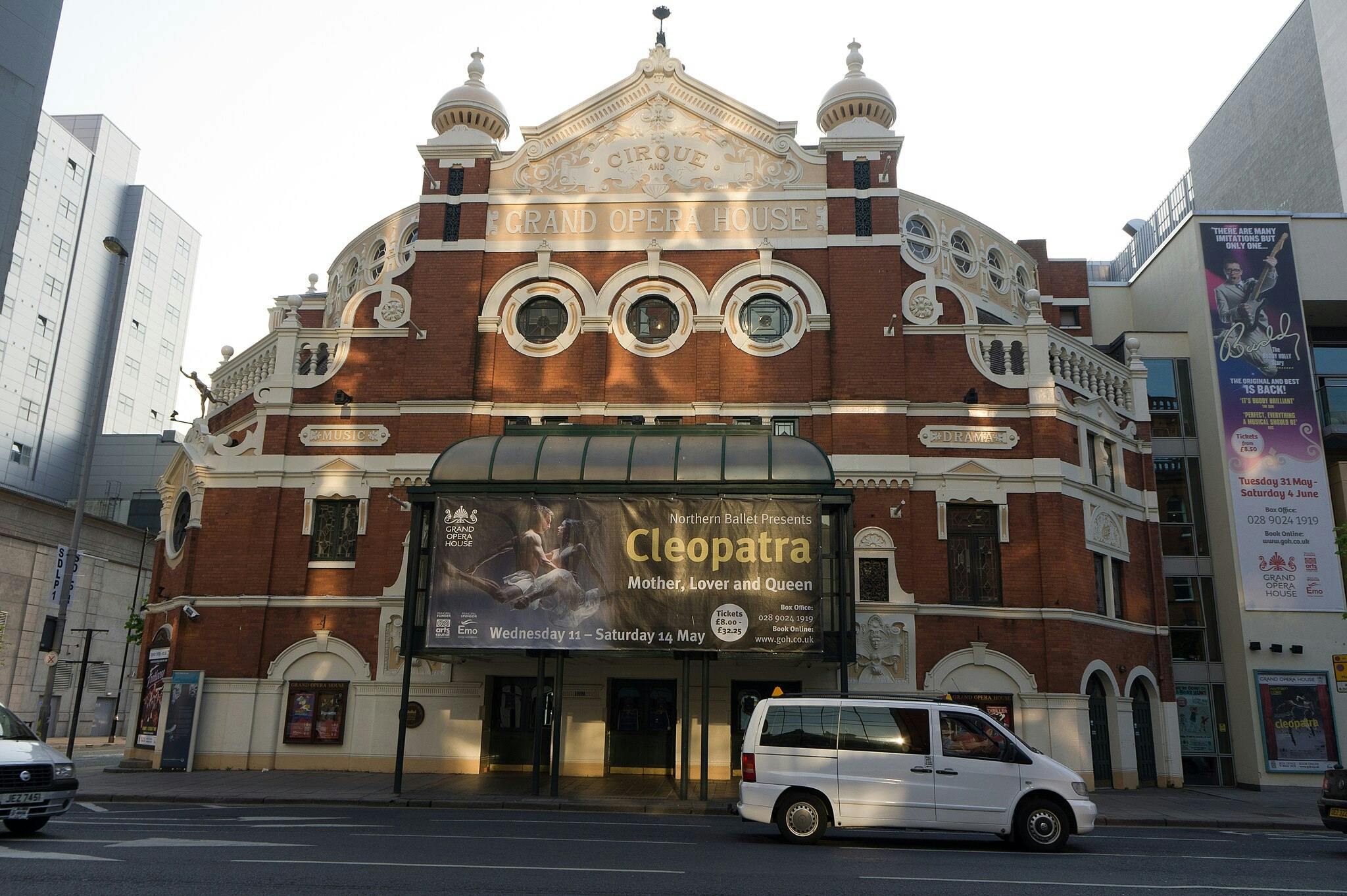 Exterior of the Grand Opera House with a marquee advertising "Cleopatra." A white van is driving past in the foreground.