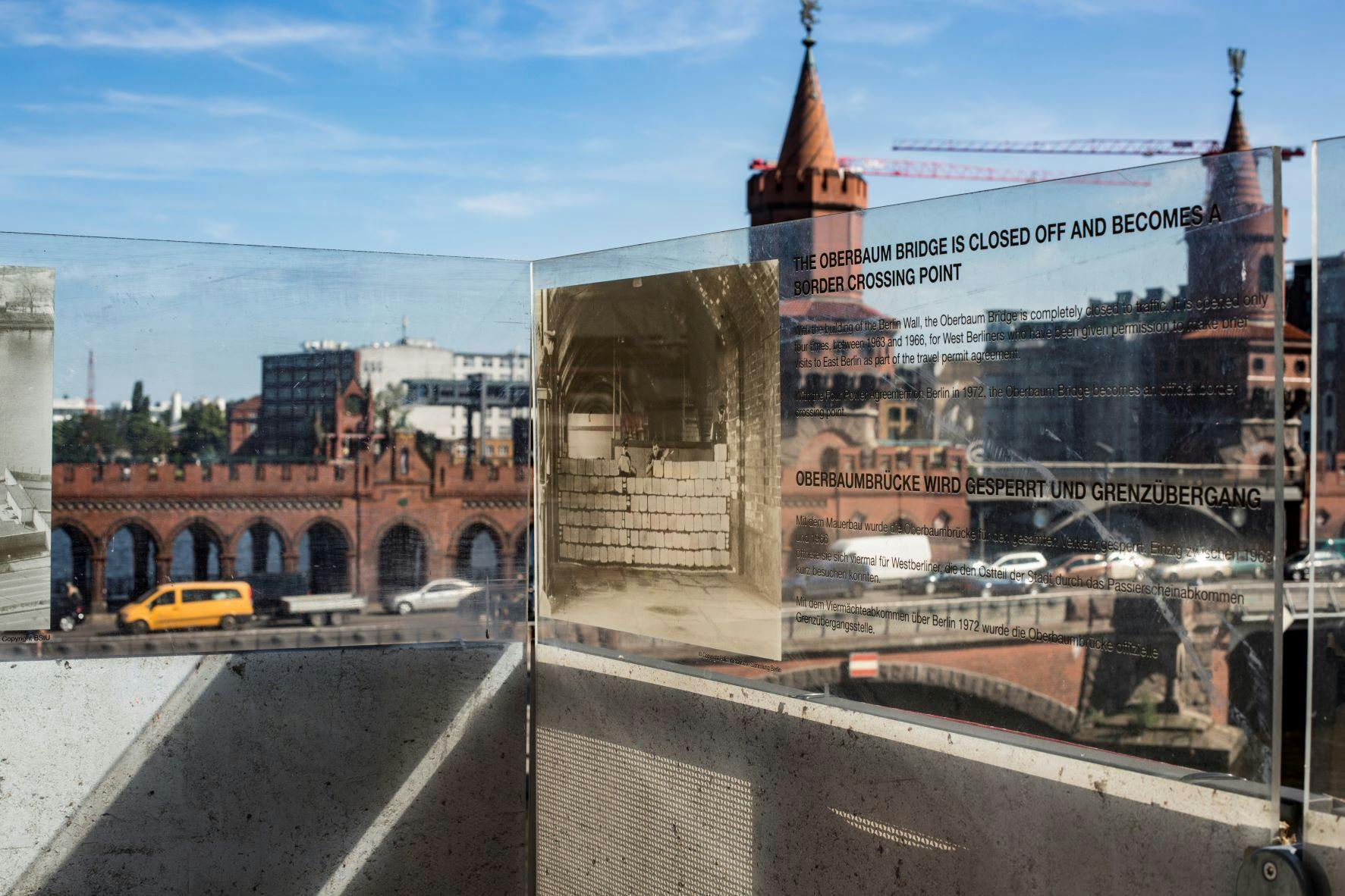 View of the Oberbaum Bridge with reflective glass displaying historical photograph and text about the bridge&#39;s closure as a border crossing.