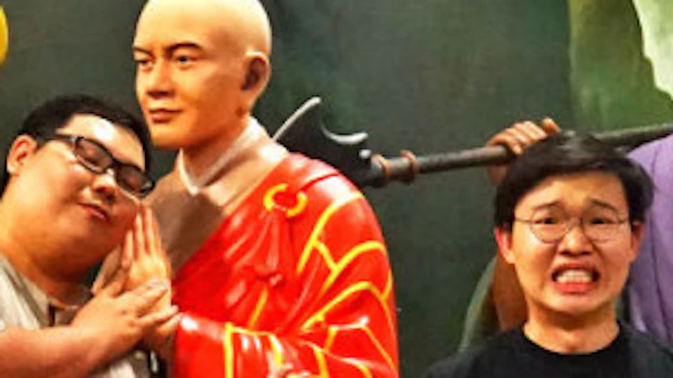 People posing humorously with realistic statues of monks and mythical characters against a mountain and sky backdrop.