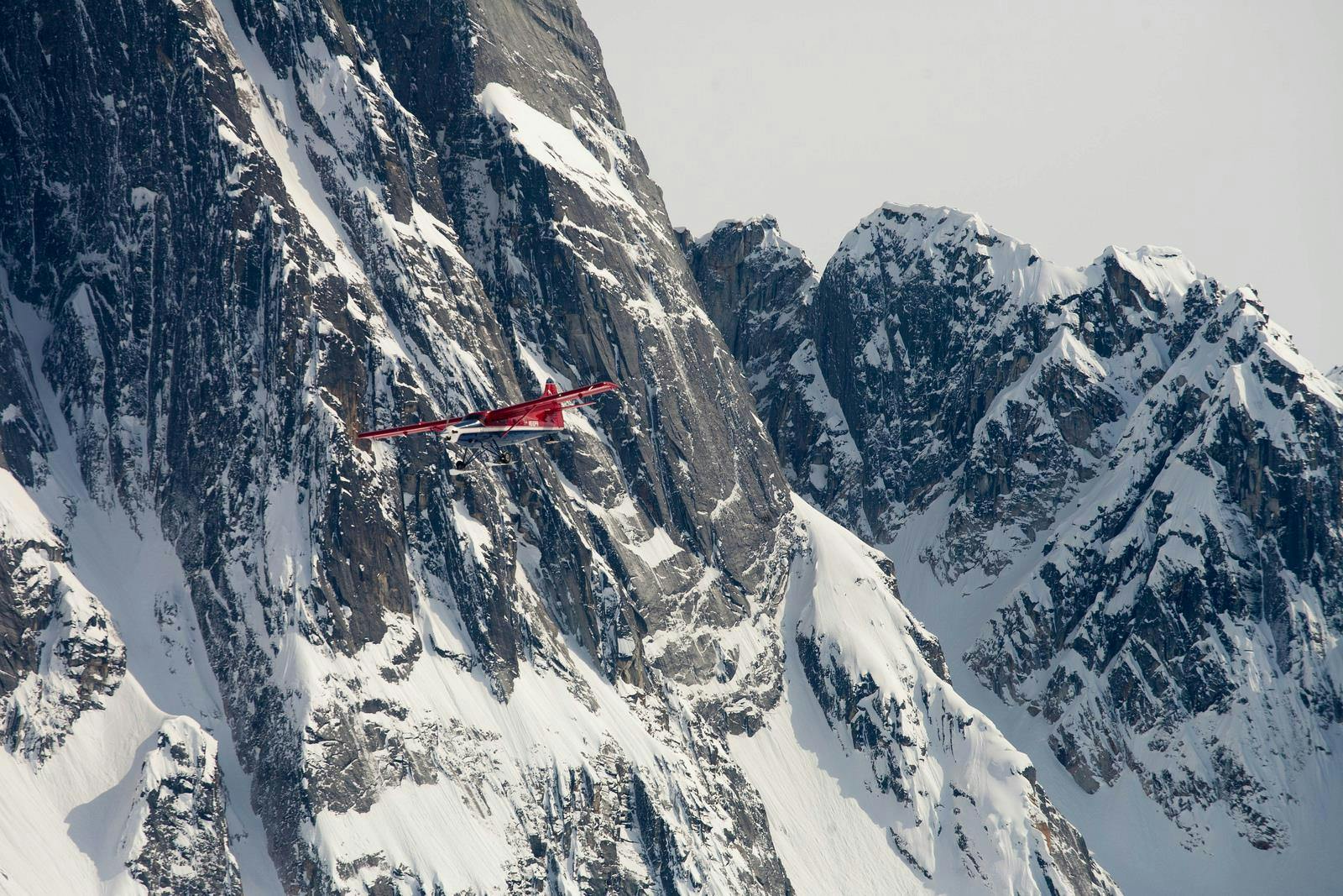 Un avion rouge volant à proximité d'imposantes falaises enneigées.