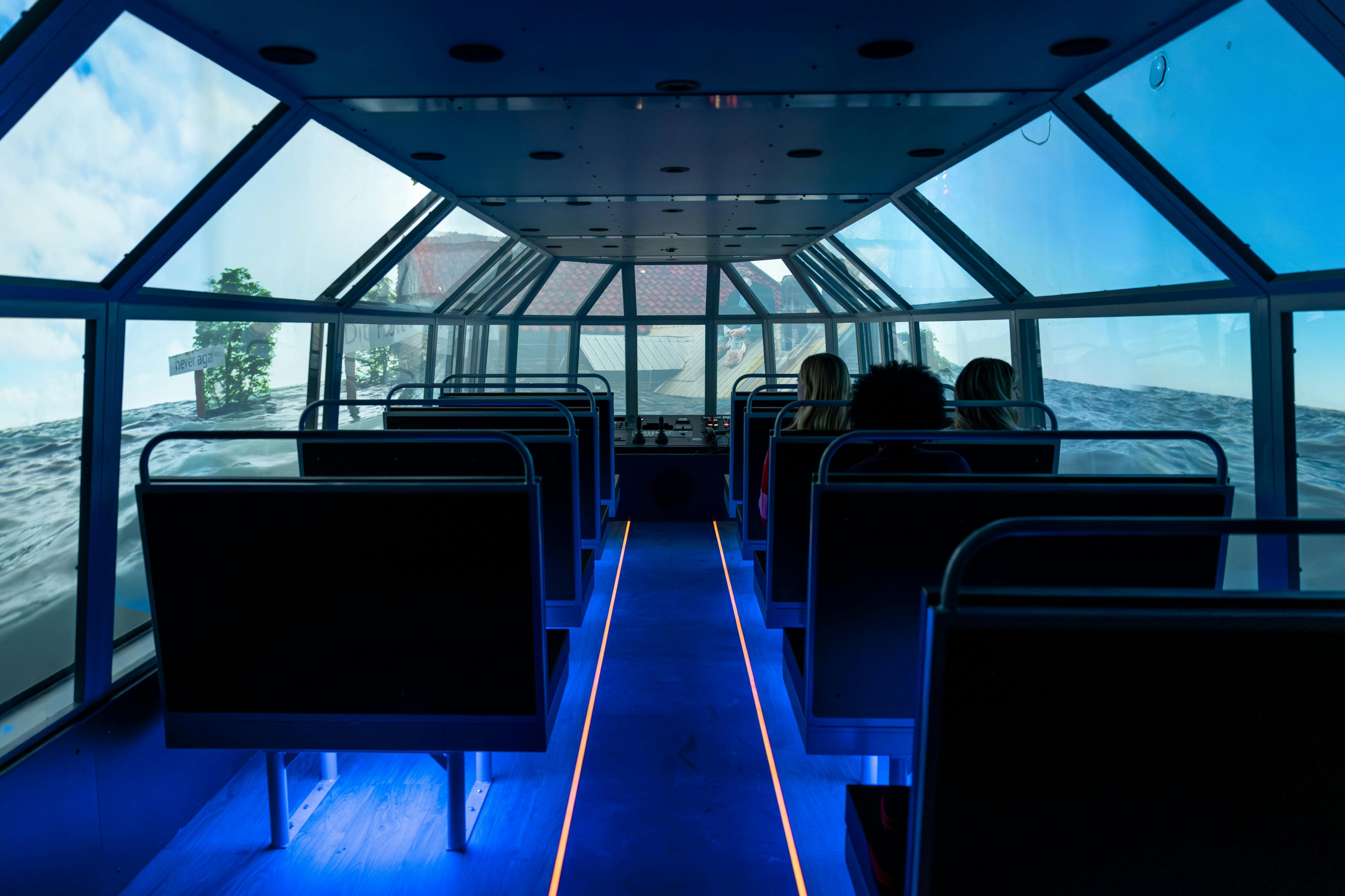 Interiör i ett simulerat fordon med sätesrader, blå golvbelysning och skärmar som visar en utomhusscen.