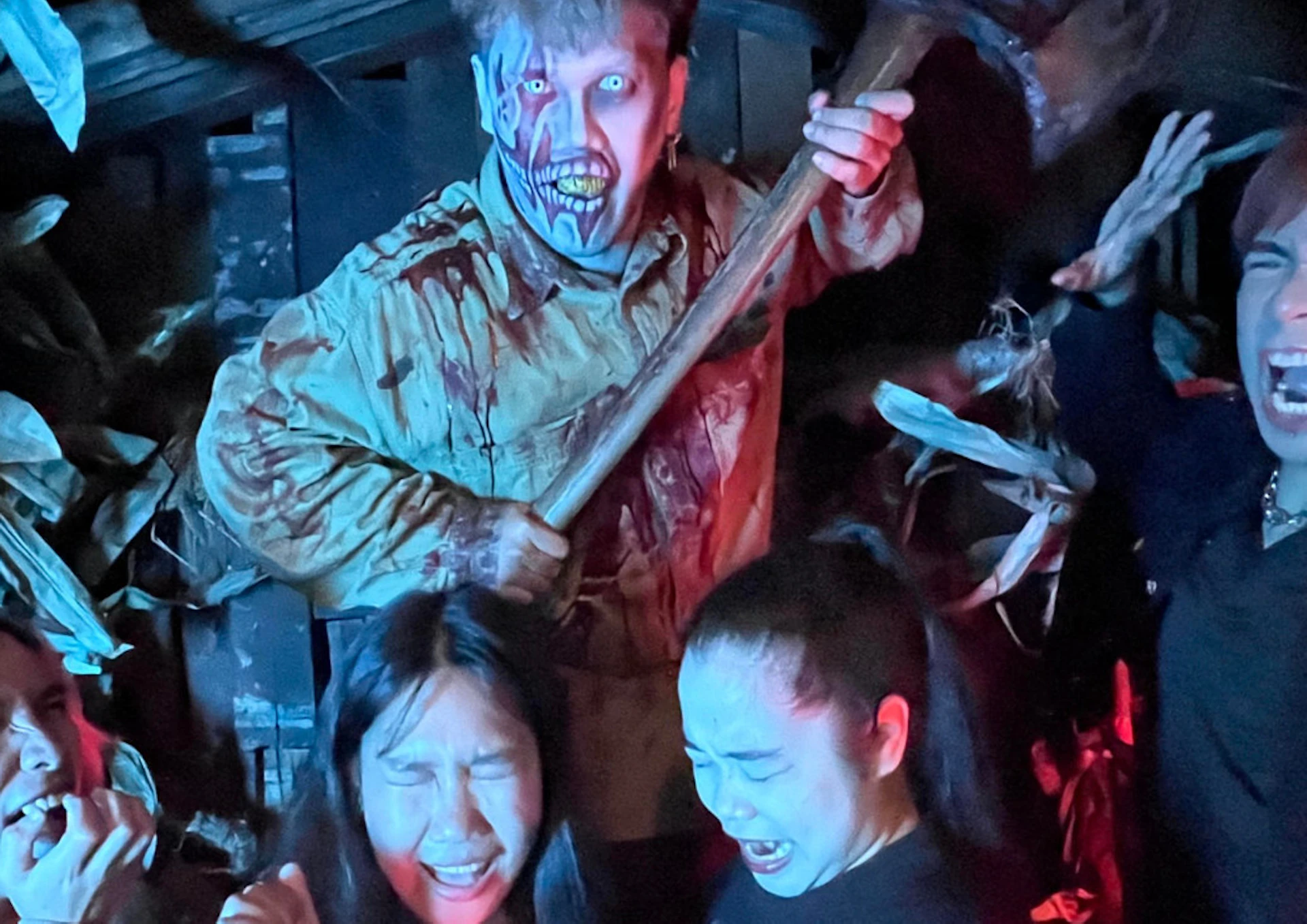 A group of people in a horror-themed setting, one in costume holding an axe, others reacting with fearful expressions.
