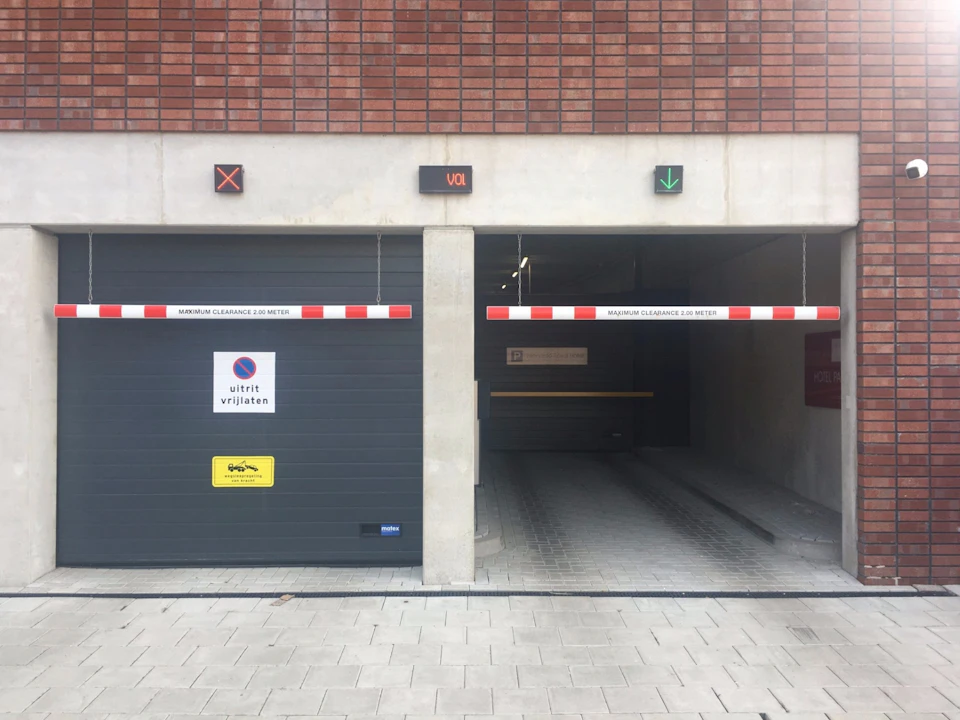 Two garage entrances with red-and-white barriers; one with a closed door and signs, the other open with a green arrow above.