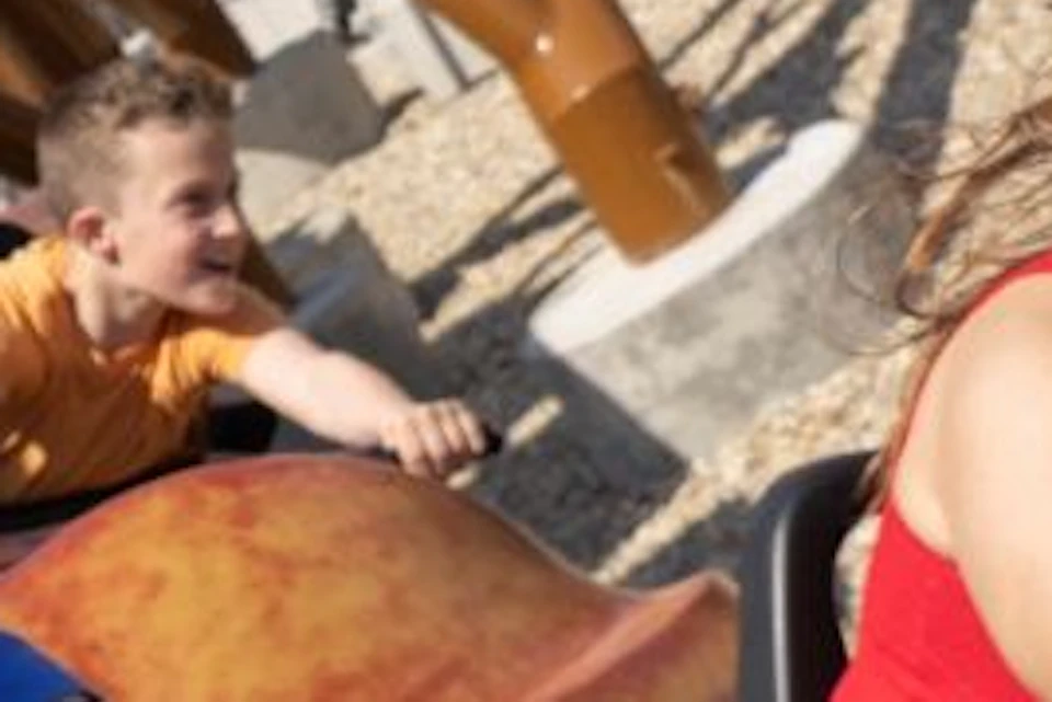 People riding a roller coaster in a park, smiling and enjoying the ride. The coaster has a brown car design.