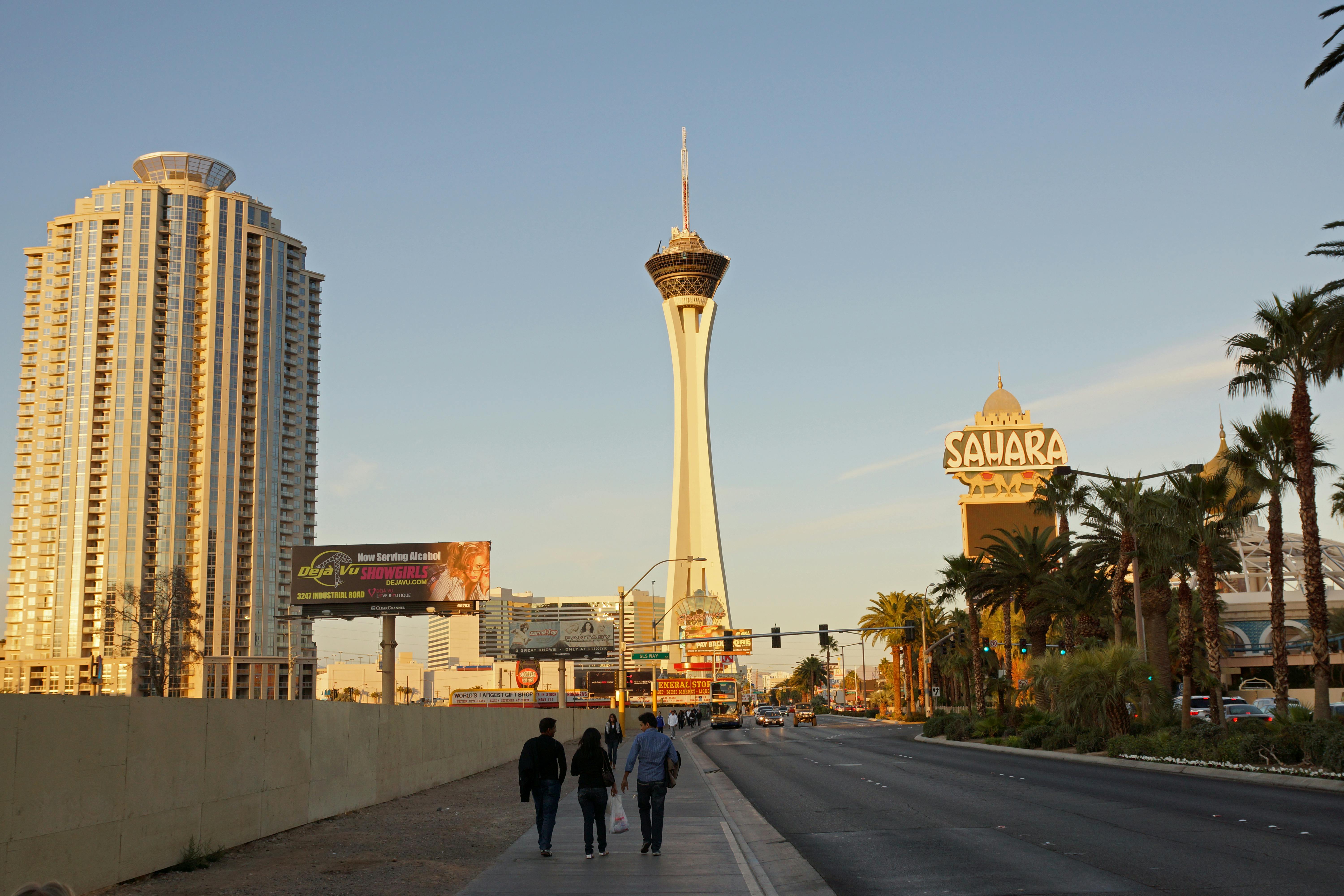 在晴朗的天空下，三个人走在人行道上，旁边有一条道路，背景是平流层塔和撒哈拉标志。