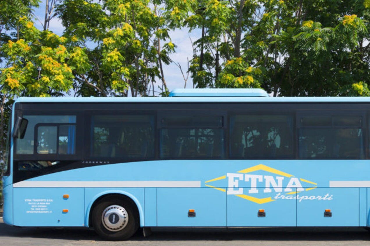 옆으로 '에트나' 라고 적힌 파란색 버스가 줄지어 있는 푸른 나무 앞에 주차되어 있습니다.