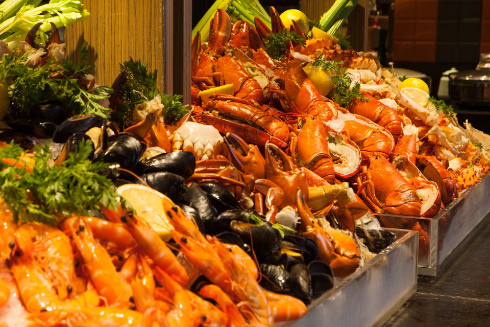 A display of assorted fresh seafood including lobsters, shrimp, mussels, and garnishes like lemon and parsley.