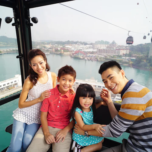 Eine vierköpfige Familie lächelt in einer Seilbahn mit Blick auf das städtische Hafenviertel im Hintergrund.