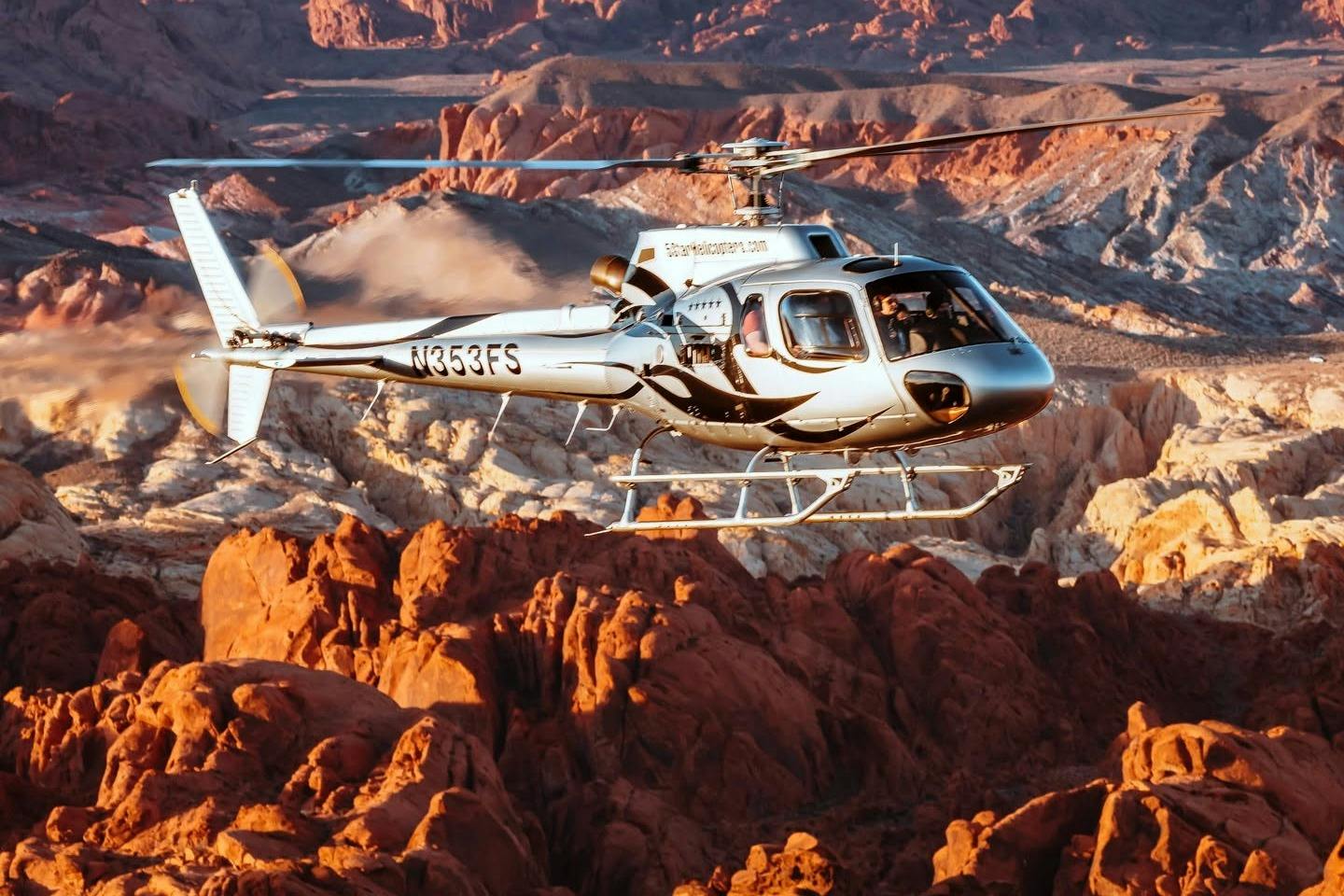 A helicopter flying over a scenic desert landscape with red rock formations and rugged terrain in the background.