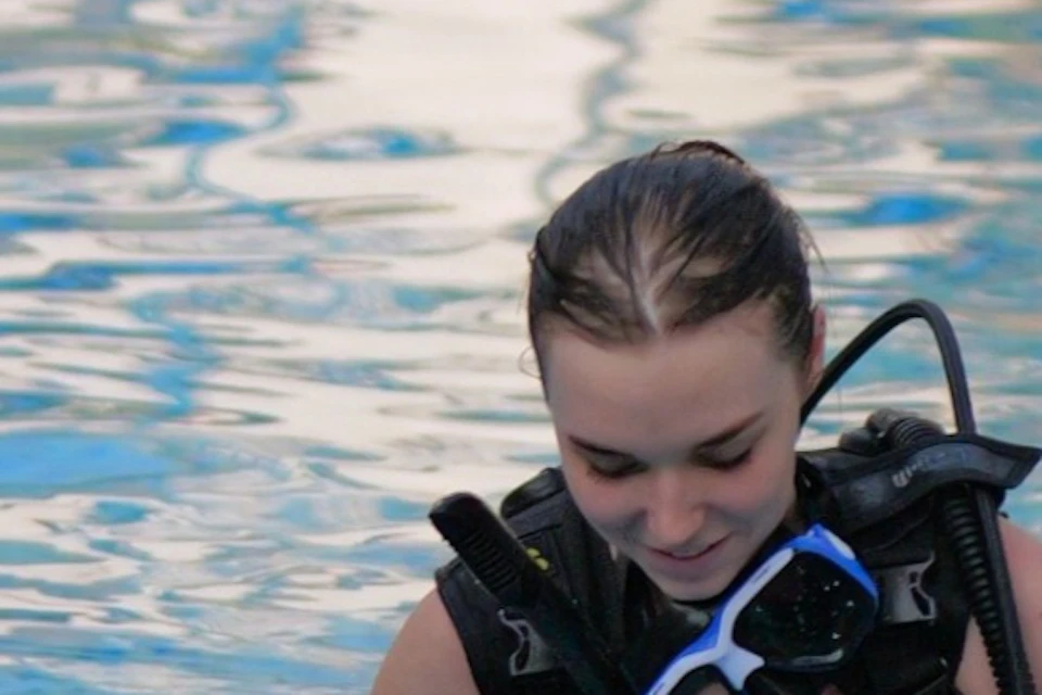Three people wearing scuba diving gear standing in a swimming pool, smiling and preparing for a dive.