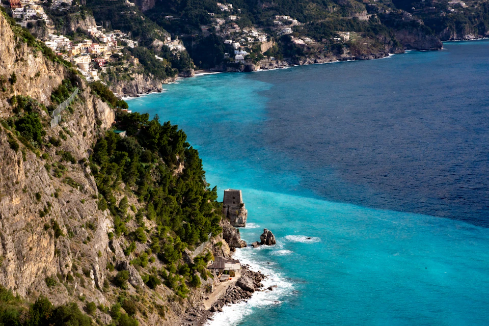 A coastline with steep cliffs covered in vegetation, turquoise water, and a small coastal structure near the shore.