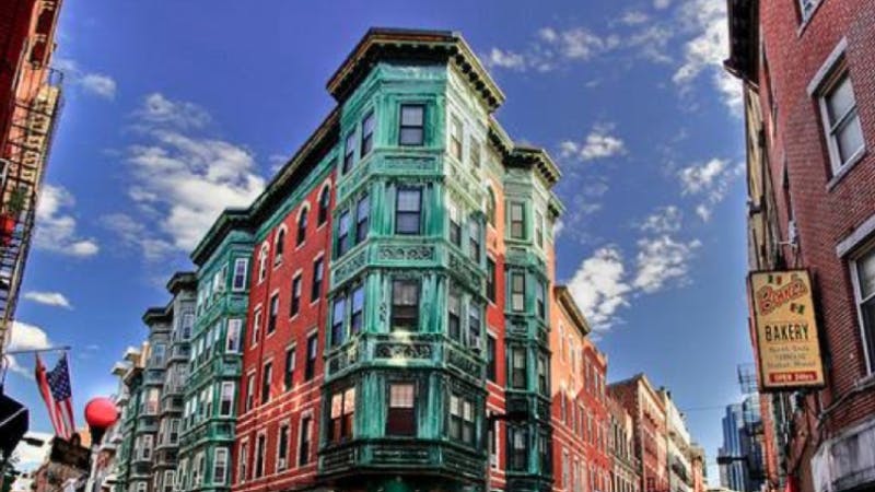 A historic multi-story building with green and red facades stands against a blue sky with scattered clouds.