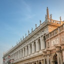 Ornate, historic building with columns, sculptures on the roof, and detailed carvings, under a clear blue sky.