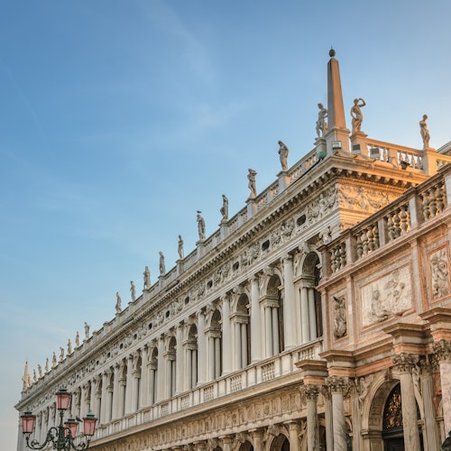 Ornate, historic building with columns, sculptures on the roof, and detailed carvings, under a clear blue sky.