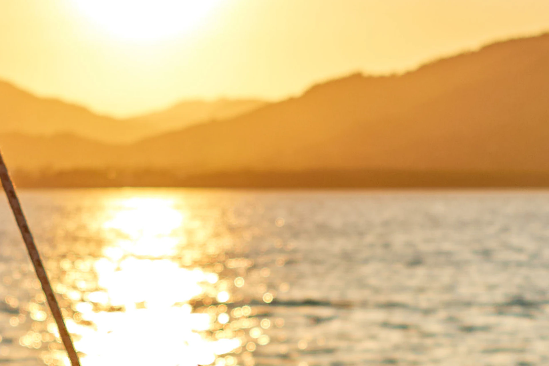 A couple on a boat at sunset, holding drinks and smiling at each other, with mountains and water in the background.