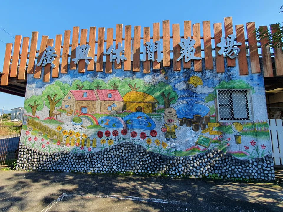 A colorful mural of a farm scene with houses, fields, and animals on a stone wall, topped with wooden slats and Chinese text.