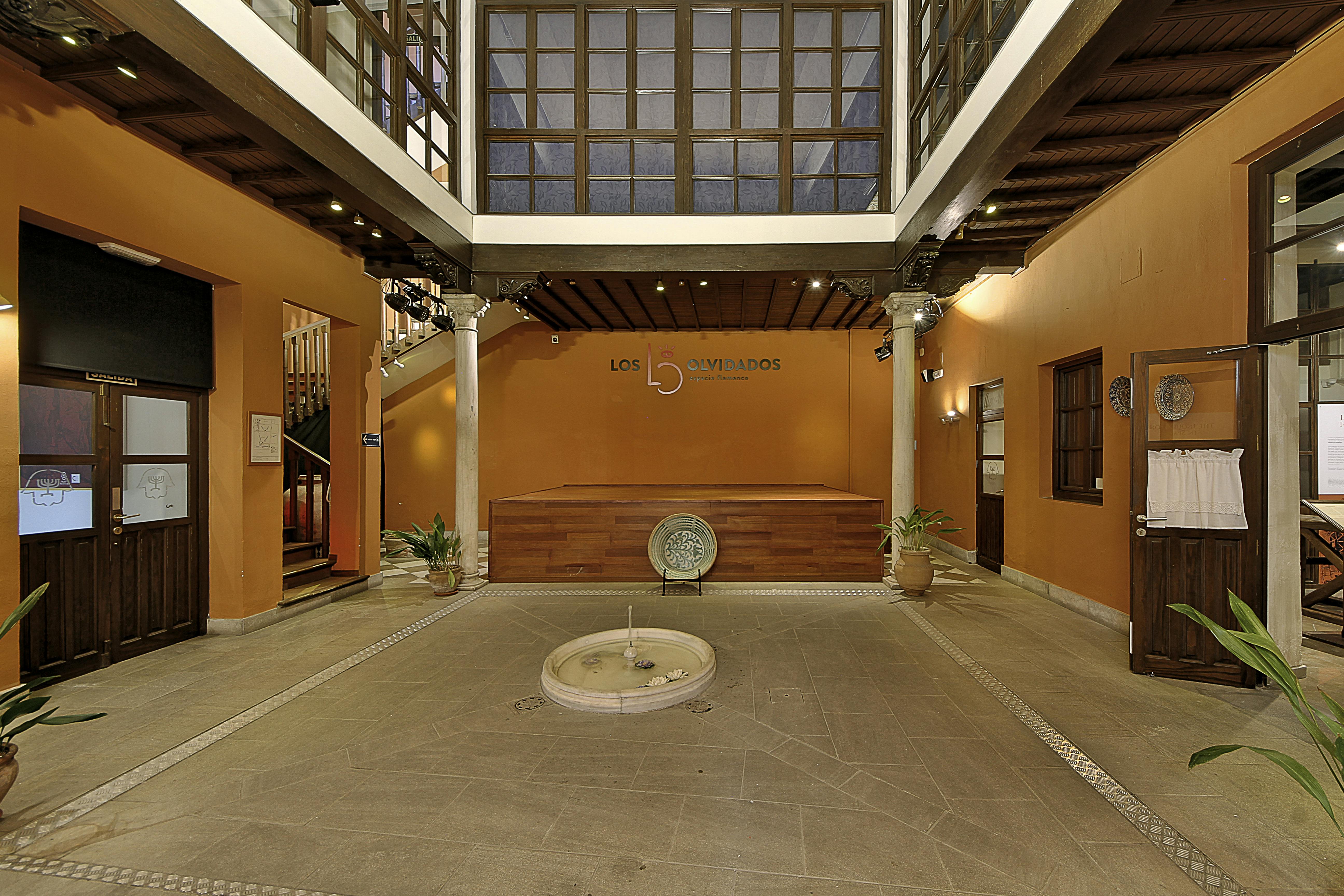 室内庭院有橙色墙壁、中央圆形喷泉、木门和盆栽植物。 墙上的“Los Olvidados”标志。