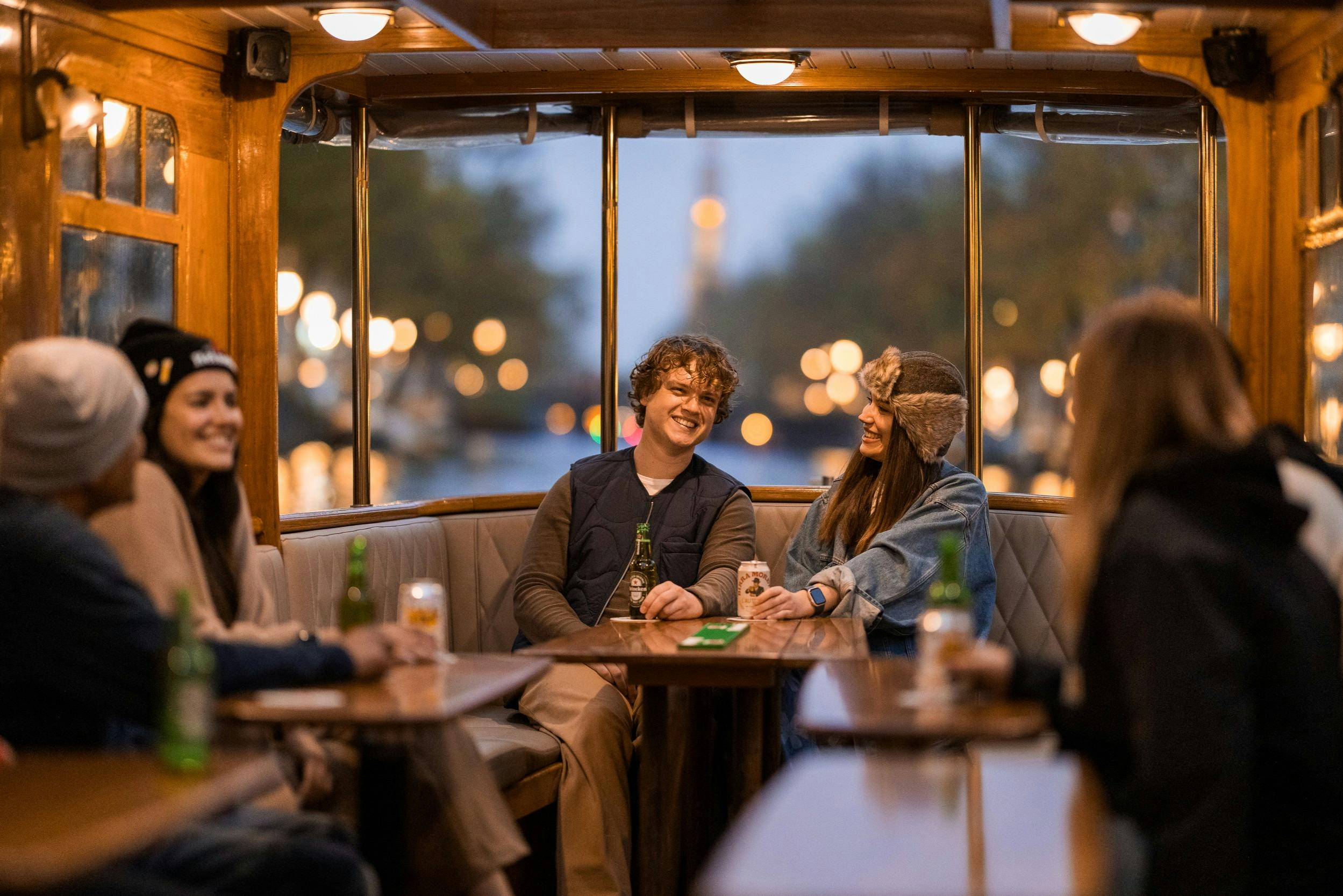 Four people sitting in a warmly lit, wooden boat cabin at dusk, laughing and enjoying drinks.