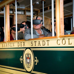 Människor som bär VR-headset sitter i en historisk spårvagnsvagn märkt "Bahn der Stadt Cöln."