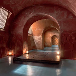 Svagt upplyst, välvd hall med rödbruna väggar och invecklade mönster, små lyktor som lyser upp den blå vattenpoolen.