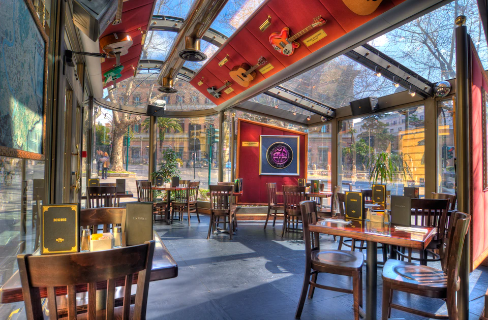 A restaurant with large windows, wooden tables and chairs, a guitar-themed ceiling, and a neon sign on the wall.