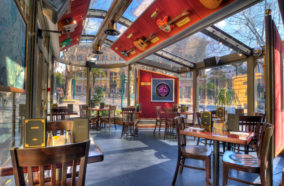 A restaurant with large windows, wooden tables and chairs, a guitar-themed ceiling, and a neon sign on the wall.