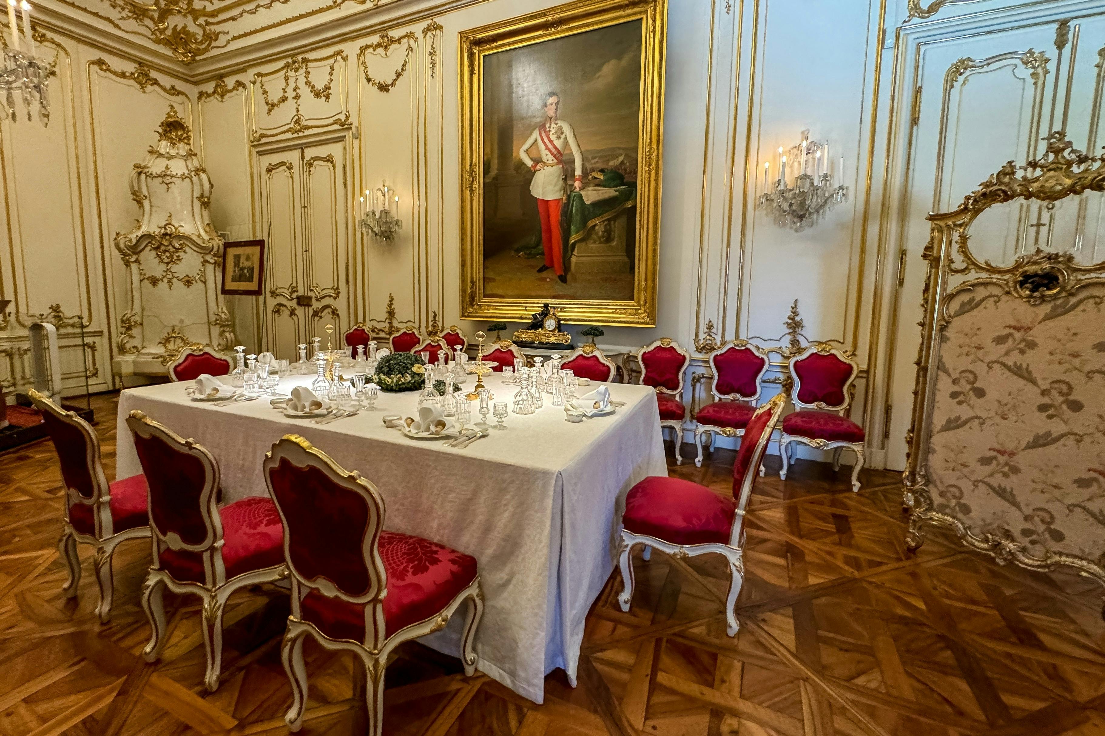 优雅的餐厅，餐桌很长，周围摆放着红色天鹅绒椅子、精致的墙壁造型和大幅肖像。