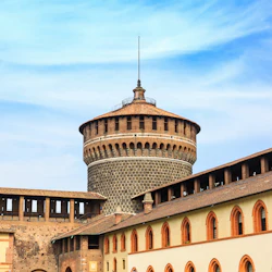 Historiskt stentorn och intilliggande tegelbyggnader under en klar, blå himmel.