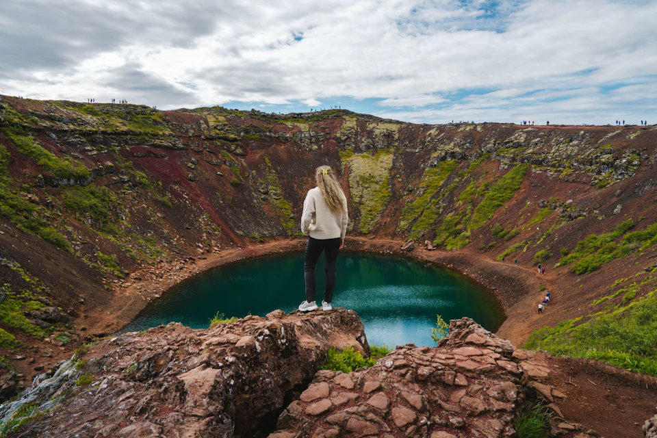 A woman standing on a rock looking at the crater and lake at the bottom
