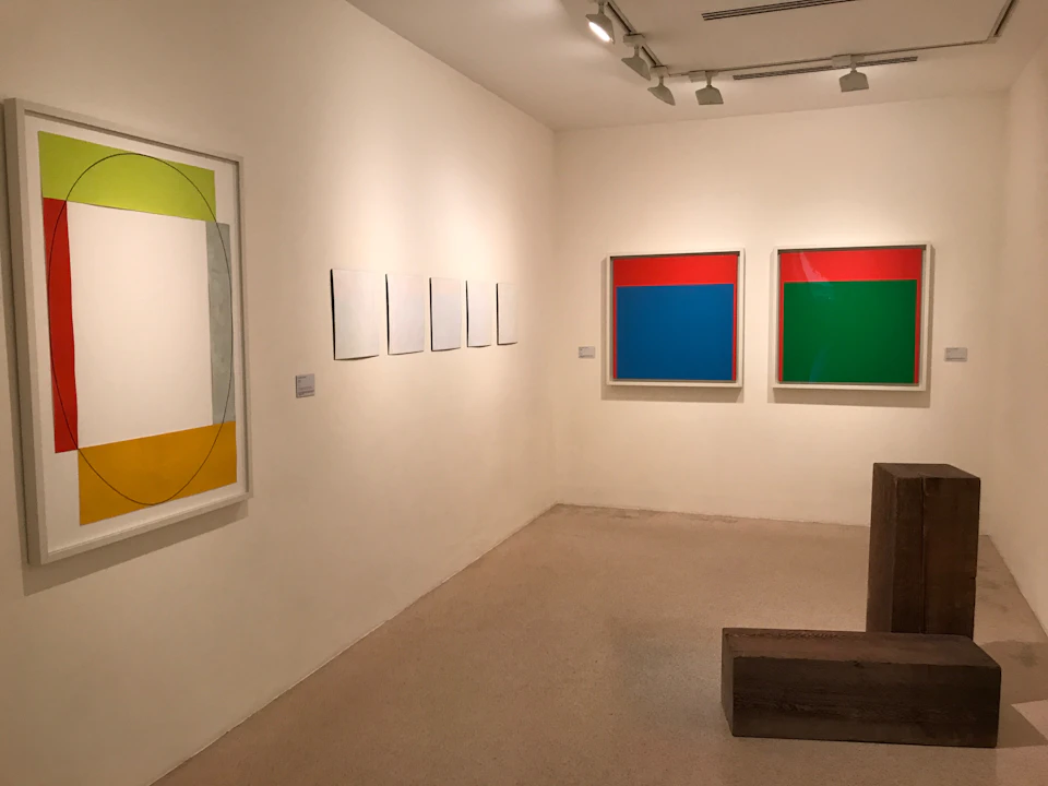 A gallery room with abstract paintings on the walls and wooden benches in the foreground.
