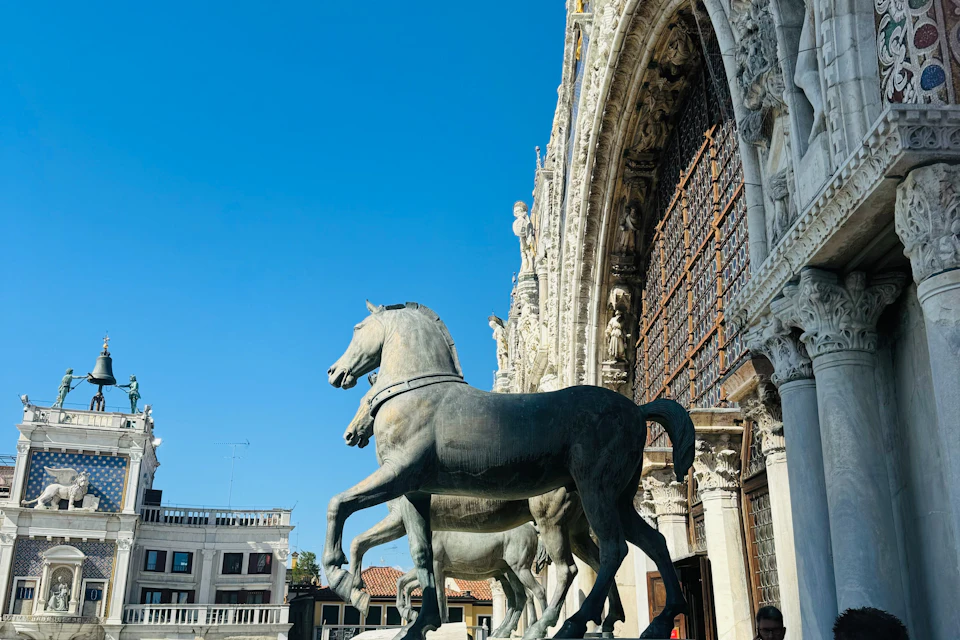 Bronze horse statues in front of a historic building with intricate architecture under a clear blue sky.