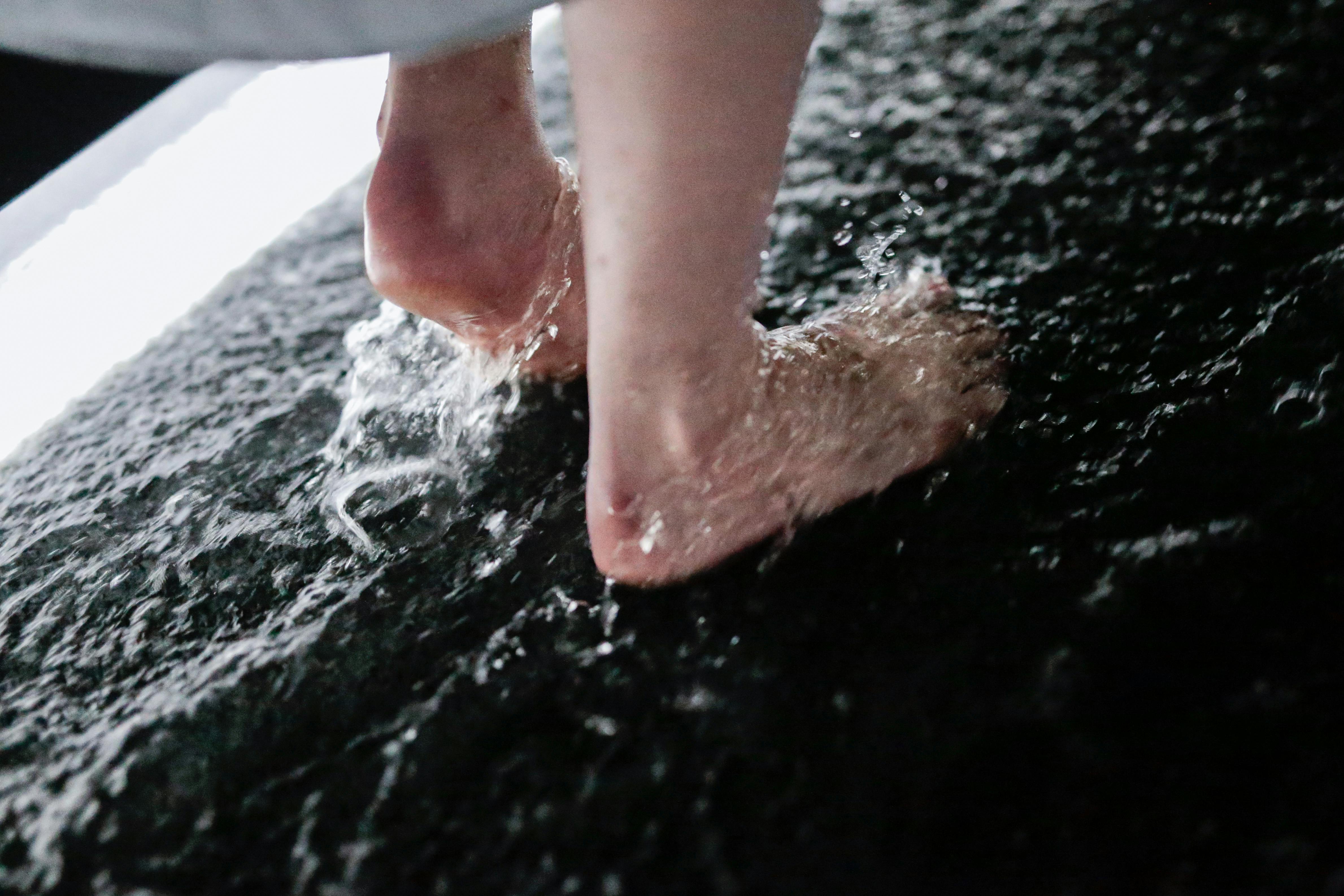 Close-up of bare feet splashing in shallow water on a textured, dark surface.