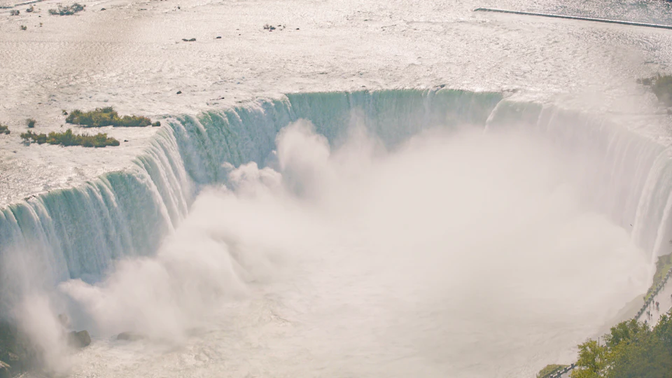 Large waterfall with water cascading over a wide edge, producing mist and clouds of spray.