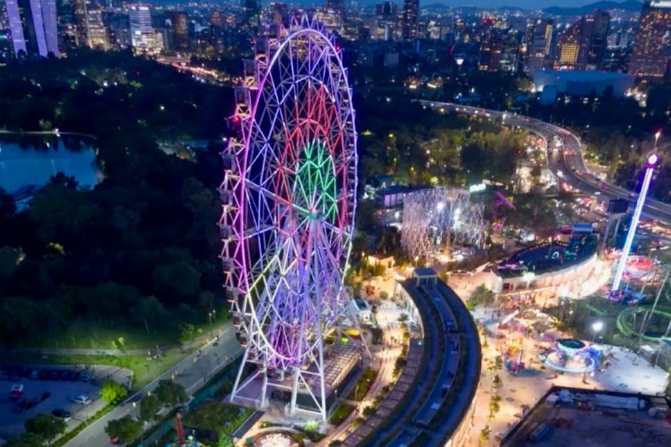 Osvětlené ruské kolo v zábavním parku v noci s městskými světly a silnicemi v pozadí.
