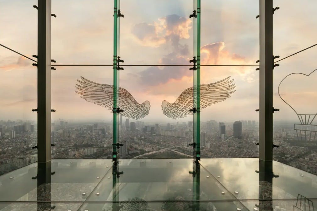 A cityscape view through a glass panel with angel wings illustration, taken from a high vantage point during sunrise or sunset.