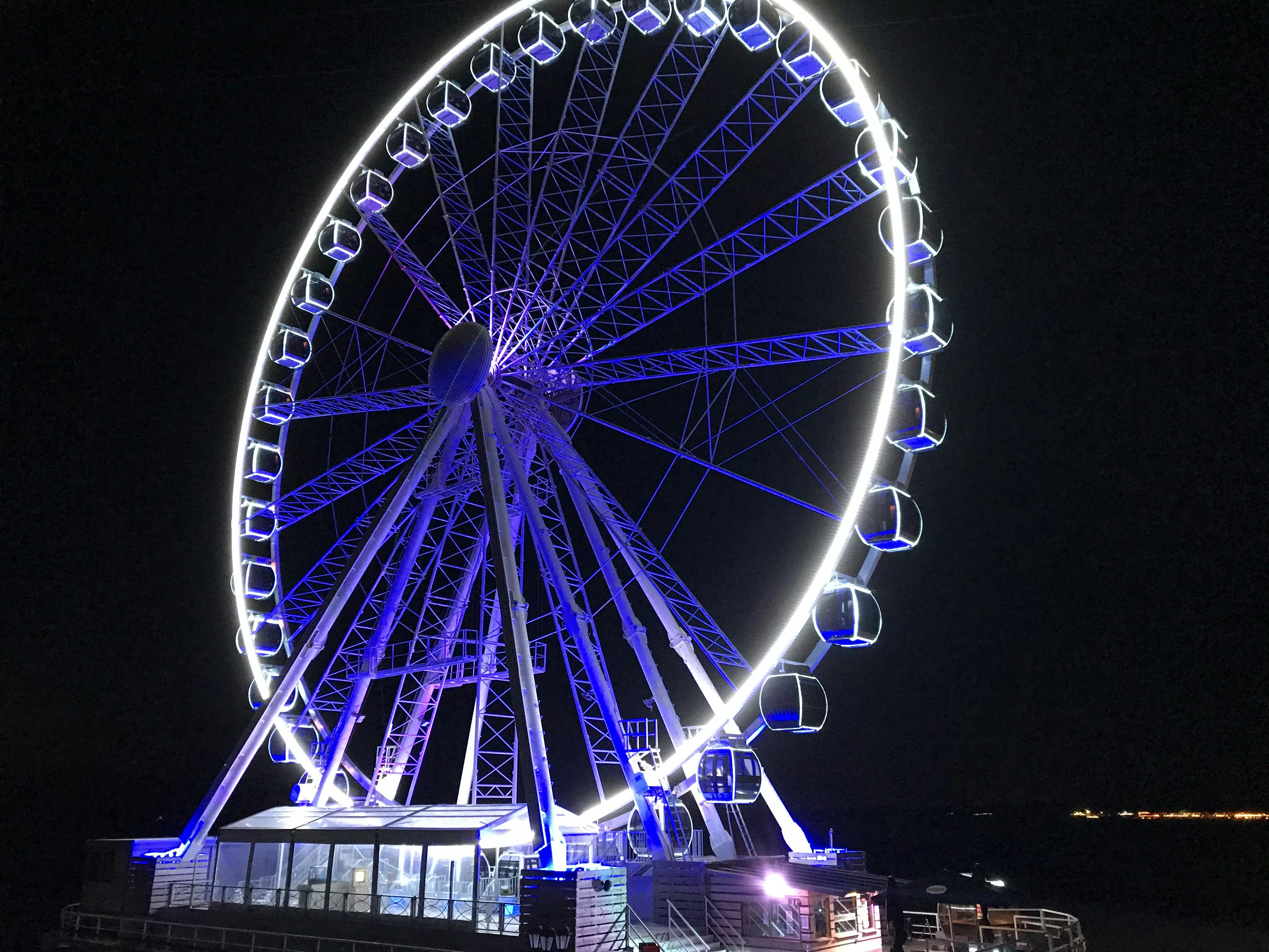 Jasně osvětlené ruské kolo s uzavřenými kajutami osvětlenými v noci modrými a bílými světly.