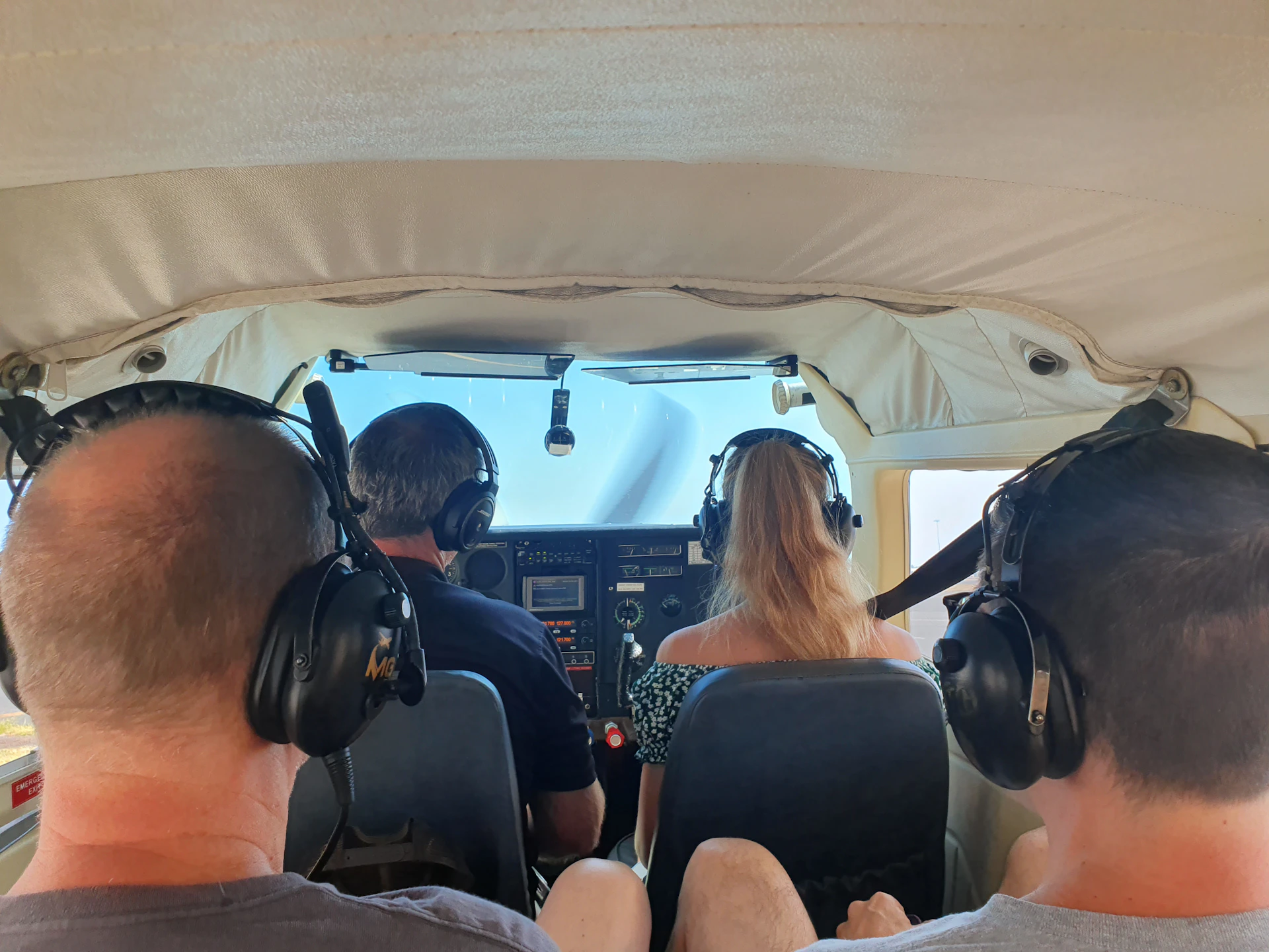 Four people wearing headsets seated in a small airplane cockpit, with a view of the controls and windows.