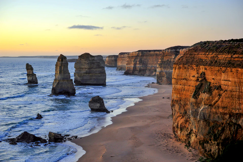 Ocean cliffs and rock formations at sunset, with waves crashing on a sandy beach.