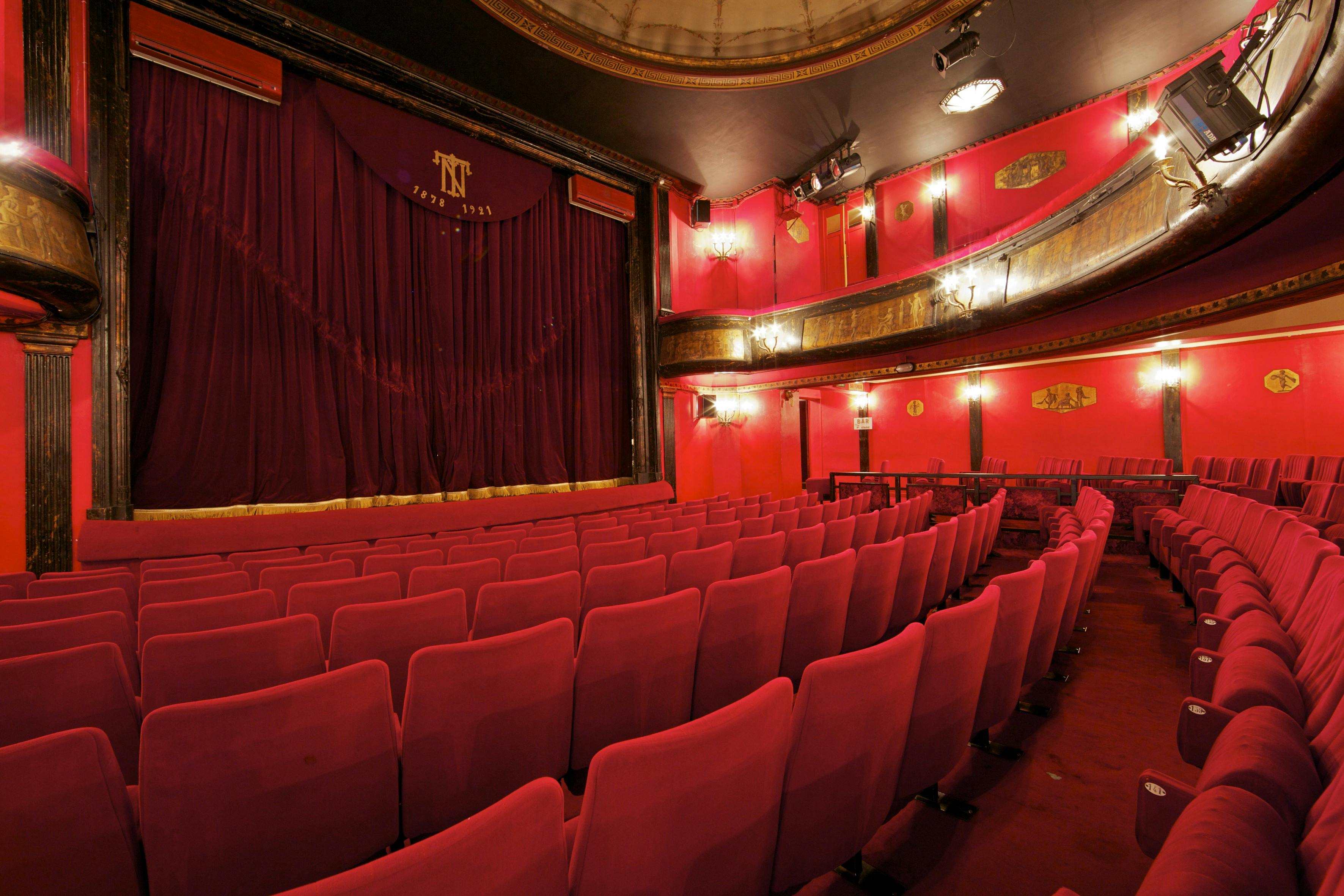 空荡荡的剧院里有一排排红色的座位，舞台上挂着红色的窗帘，墙壁和阳台上摆放着华丽的红色和金色装饰。