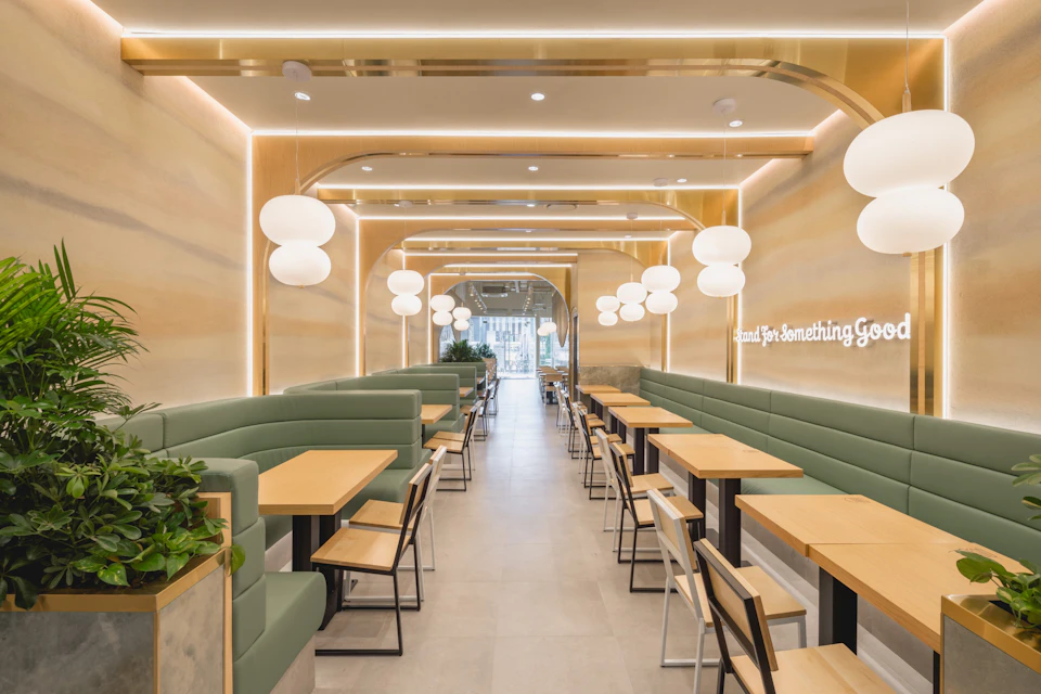 Modern restaurant interior with green booths, wooden tables, white chairs, pendant lights, and a bright, minimalist design.