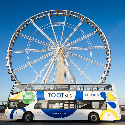 En dubbeldäckad Tootbus med "Planet Friendly" -märkning står parkerad framför ett stort pariserhjul i Bryssel under en klarblå himmel.