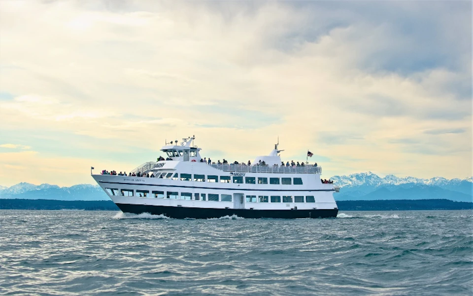 Argosy Cruise boat with Olympic Mountains in the background, with people visible on the outer decks.