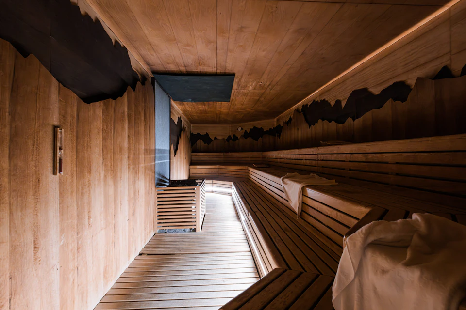A modern wooden sauna interior with bench seating along the walls and towels placed on them.