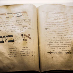 Ett öppet gammalt manuskript med hebreisk text, utsmyckade stora bokstäver och dekorativa element på åldrade, gulnade sidor.