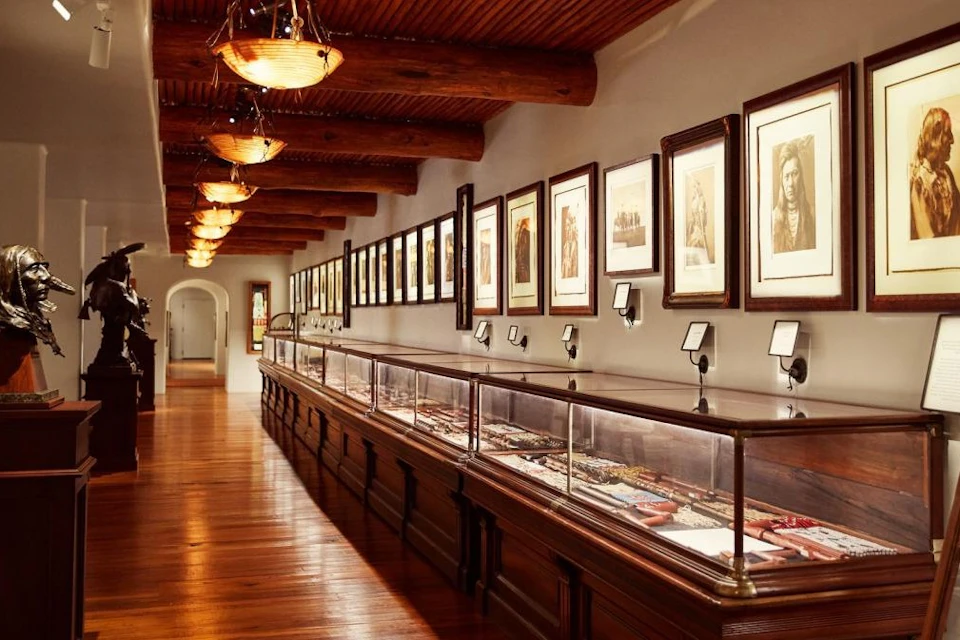 A museum gallery with wooden floors, framed artwork on the walls, and glass display cases containing artifacts.